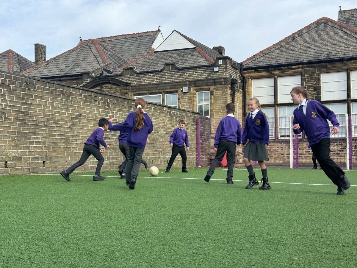 A large group of primary school children are playing football on a MUGA installed by Pentagon Play.