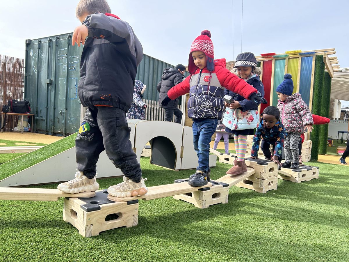 A group of toddlers are balancing across the Play Builder planks.#