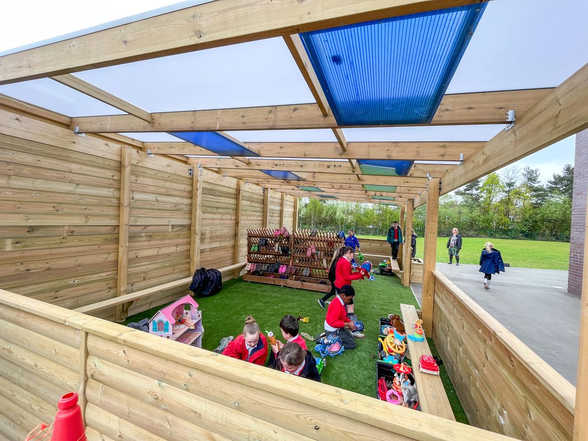 A group of children are sat underneath a freestanding canopy that has coloured plastic windows on the roof.
