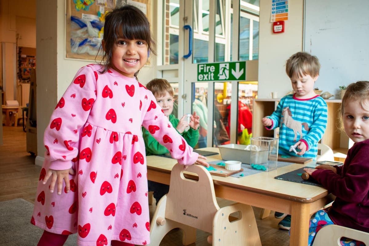 A little girl is pulling out a Millhouse chair from a desk as she looks at the camera and smiles.
