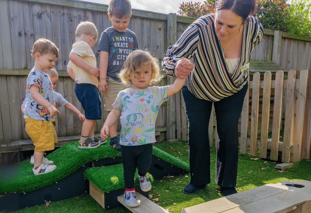 An EYFS Teacher is holding hands with a little child as they navigate their way through the course.