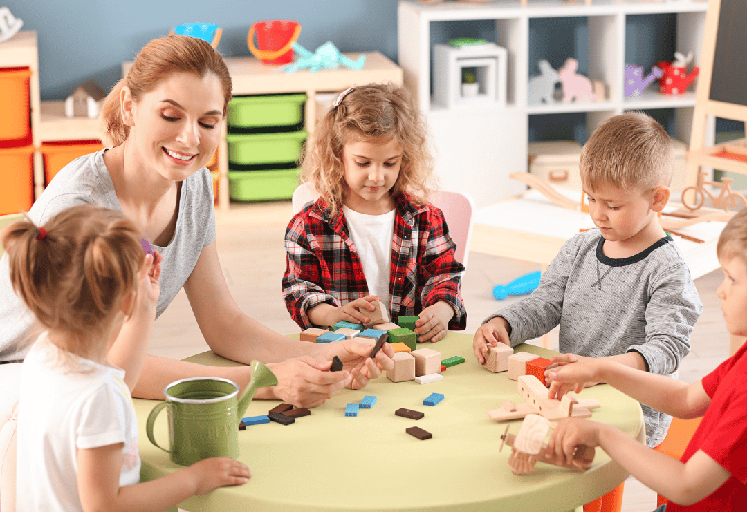 4 Children are sat at a table with an early years teacher as they take part in arts and crafts.