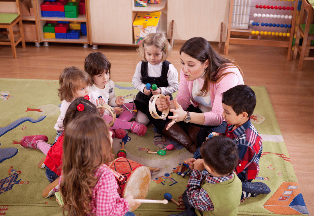 An early years teacher is sat on the floor with her children as they play musical instruments in a circle.