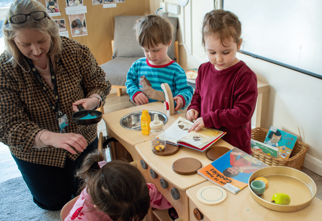 An Early Years Teacher sat with a group of small children during role play session.