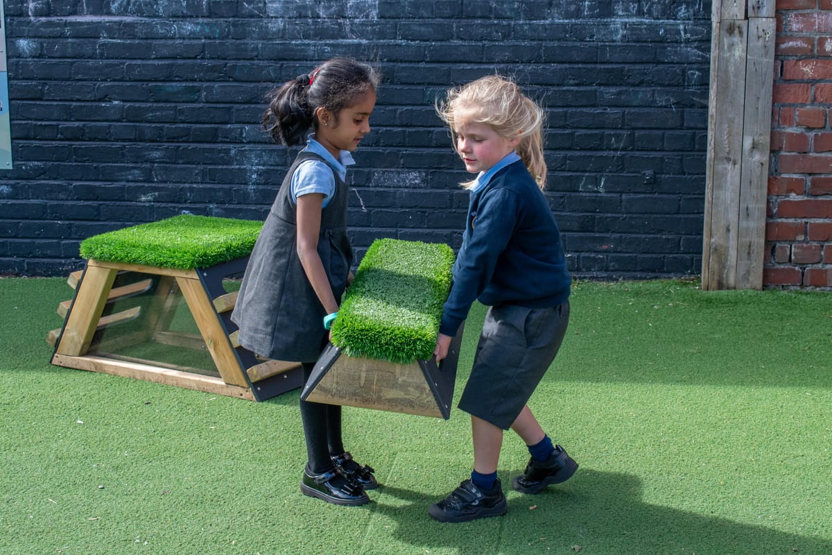 Two little girls in school uniform are moving a get set go block on a playturf surface.