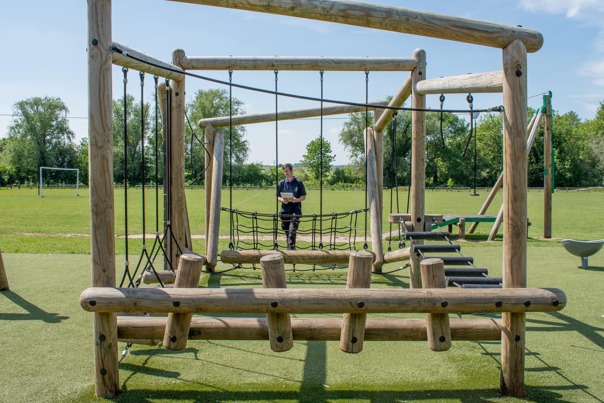 A playground inspector is checking the structural strength of a trim trail, ensuring that it's safe.