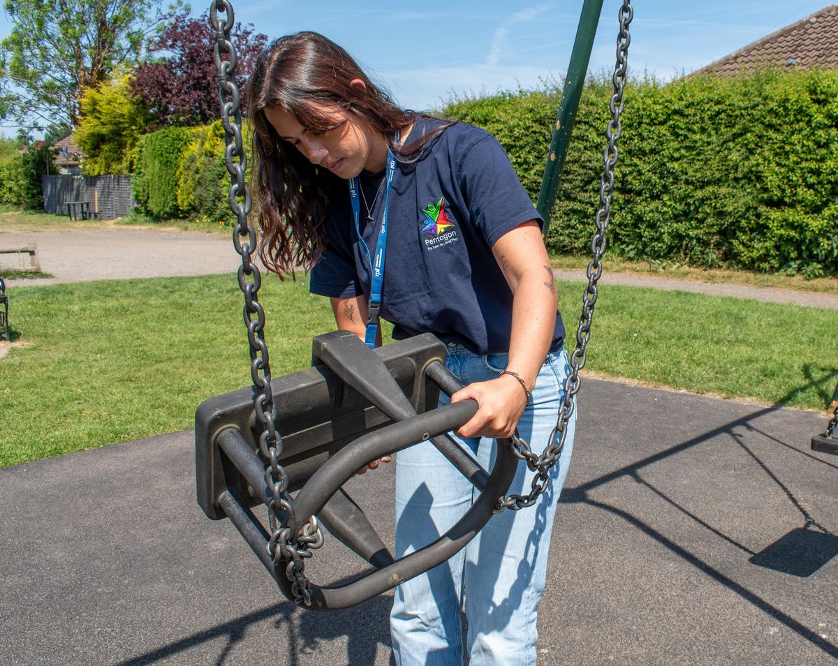 A playground inspector is looking underneath a swing for any missing parts.