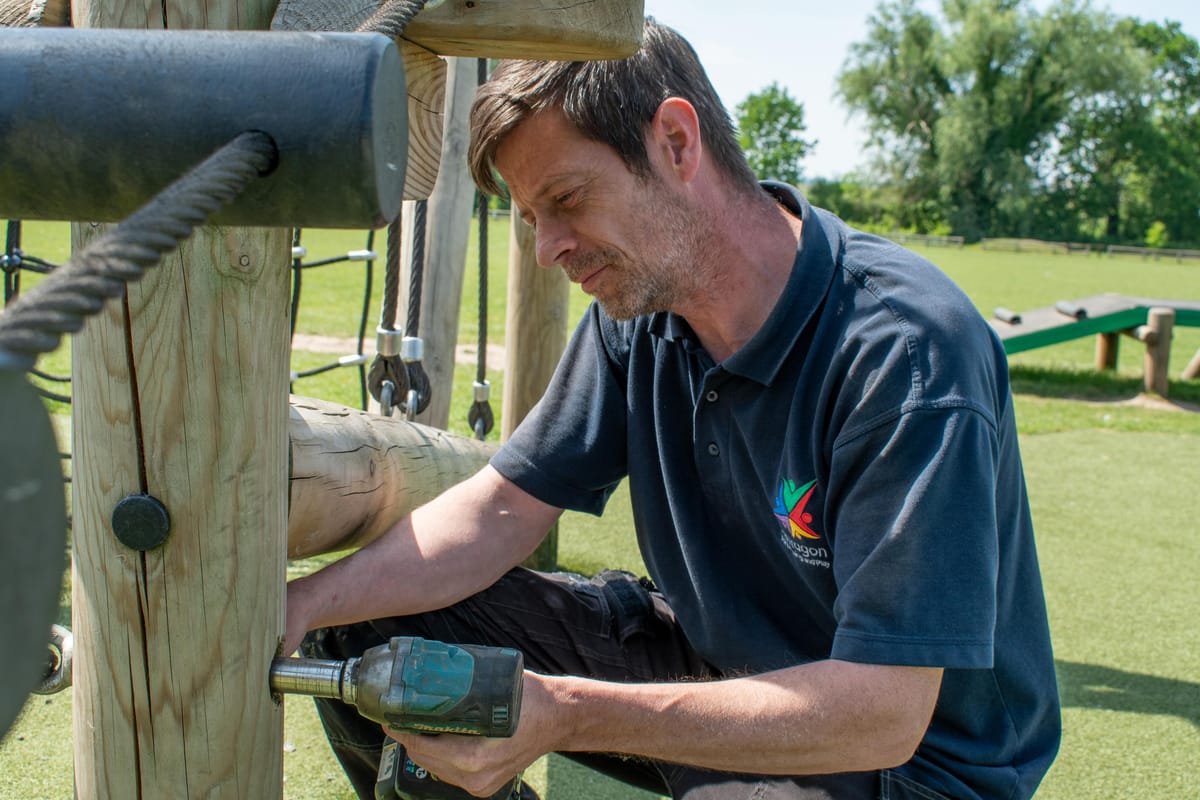 A playground inspector is tightening a loose bolt for a piece of play equipment.
