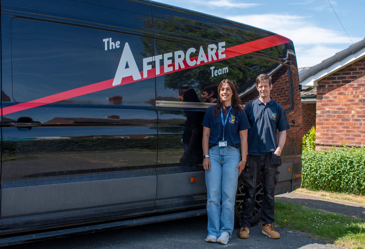 Two playground inspectors are stood beside the Aftercare van and are looking at the camera and smiling.