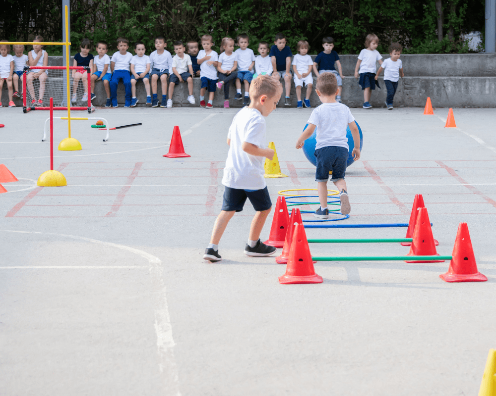 Two children are moving sports equipment around on the playground.