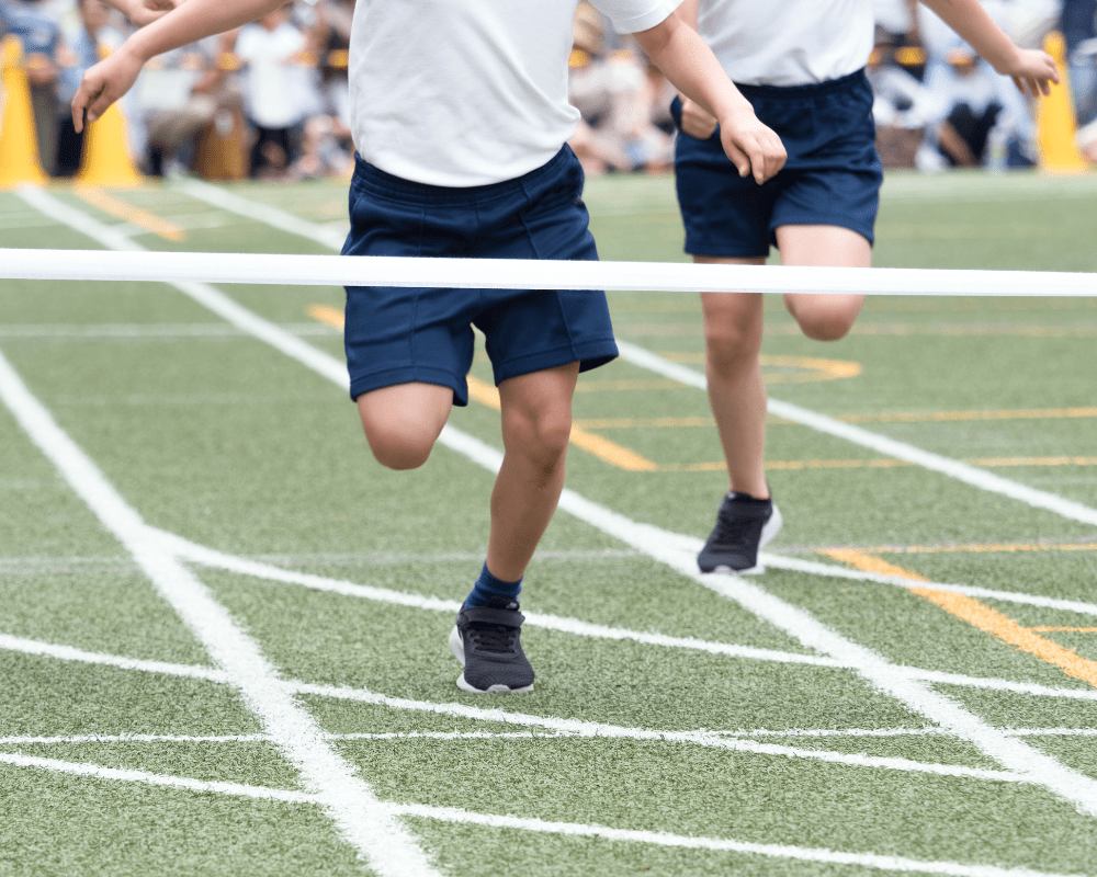 Two children are running towards the camera, which has a finish line tap in front of it.