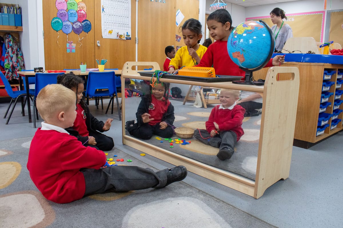 Two children are sat in front of a mirror as they play with toys.