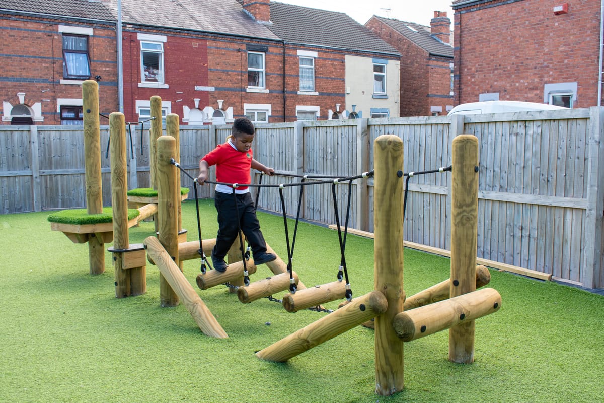 A young boy is crossing a wooden step bridge that has been installed on artificial grass.