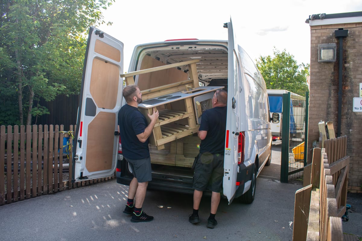 Two Pentagon Play installers are moving a piece of movable play equipment out of a van, as they deliver the equipment.