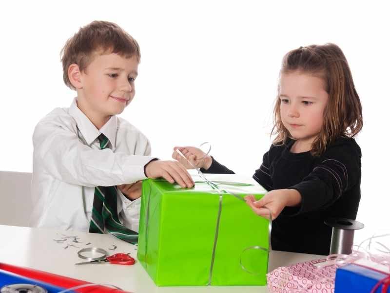 Two children are wrapping a green present up, whilst in school uniform.
