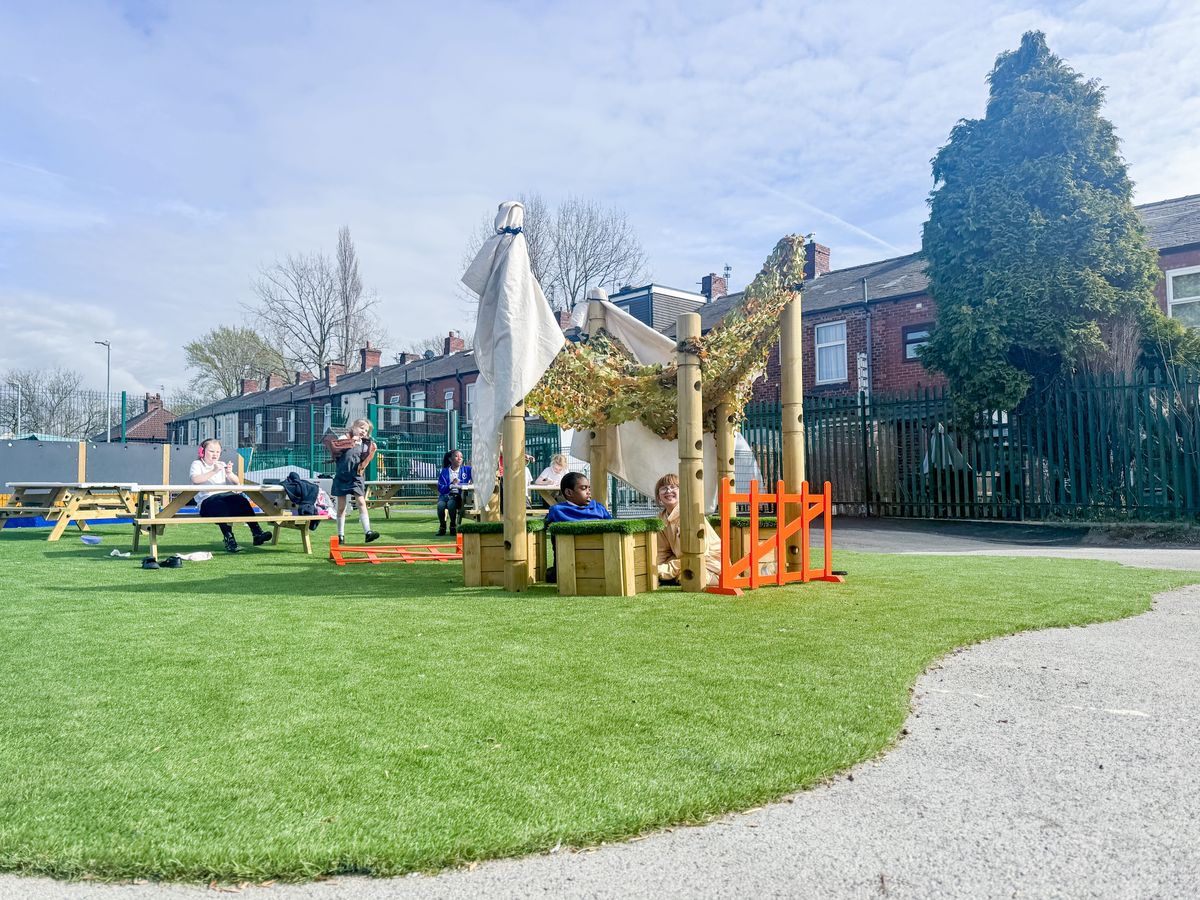 A child with EBSA and a member of support staff are sat beneath a den that has been built with Pentagon Play's Den Building posts.