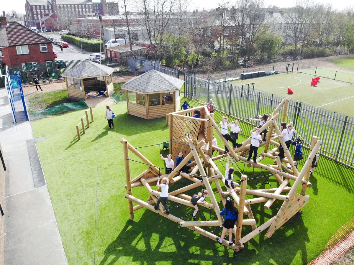 A large group of children are playing on a climbing frame on artificial grass.