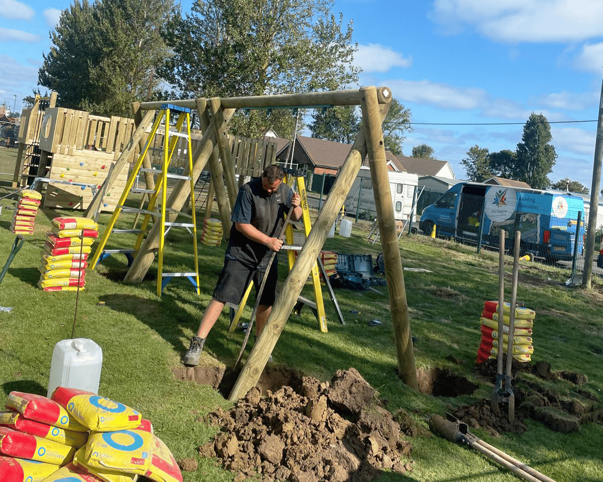 An installer is placing the swing poles into the ground, ensuring the structure is safe.