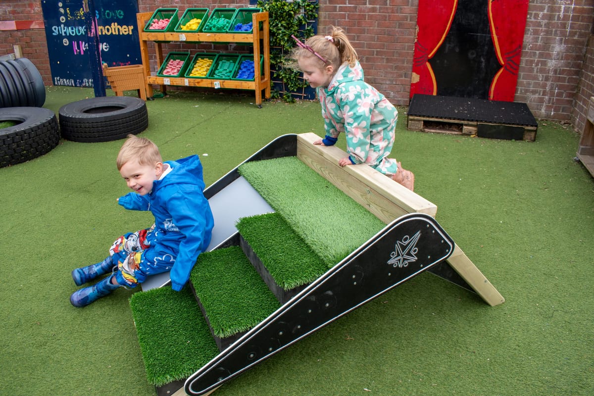 Two children are playing with the A-frame Climb & Slide, a new piece of play equipment designed for Sports Premium funding.
