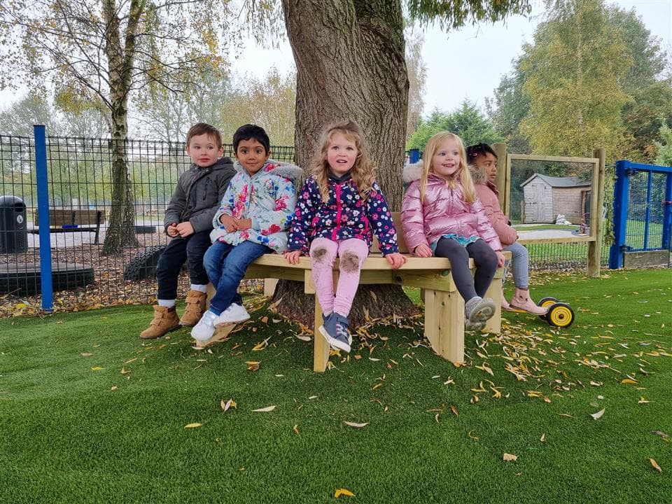 4 children sat on their tree bench with artificial grass surrounding it.