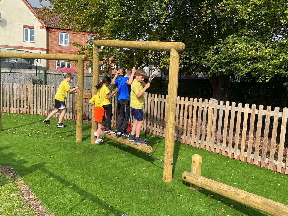 children crossing the wobbly log traverse as they help each not to fall below onto the shockpad and wetpour surfacing