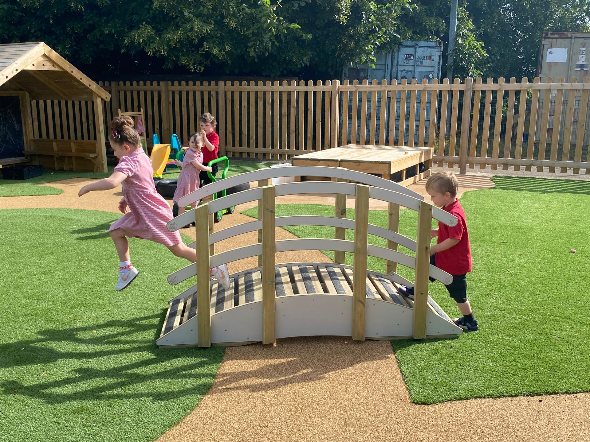 2 children playing on the play bridge in their playground whilst two other children watch from the side, they are wearing their school uniform