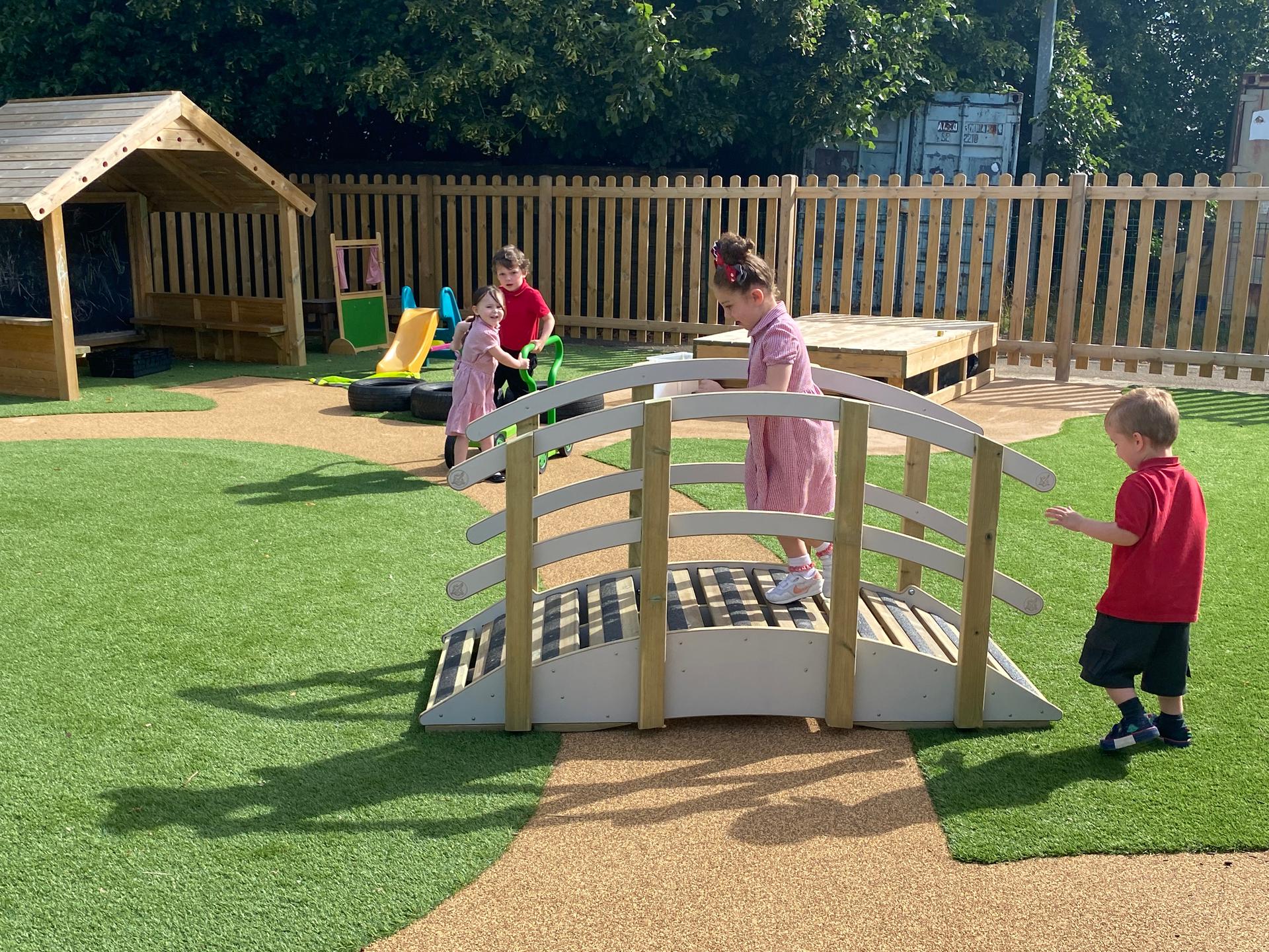 Two children walking across the playridge whilst two children are in the background smiling at them.