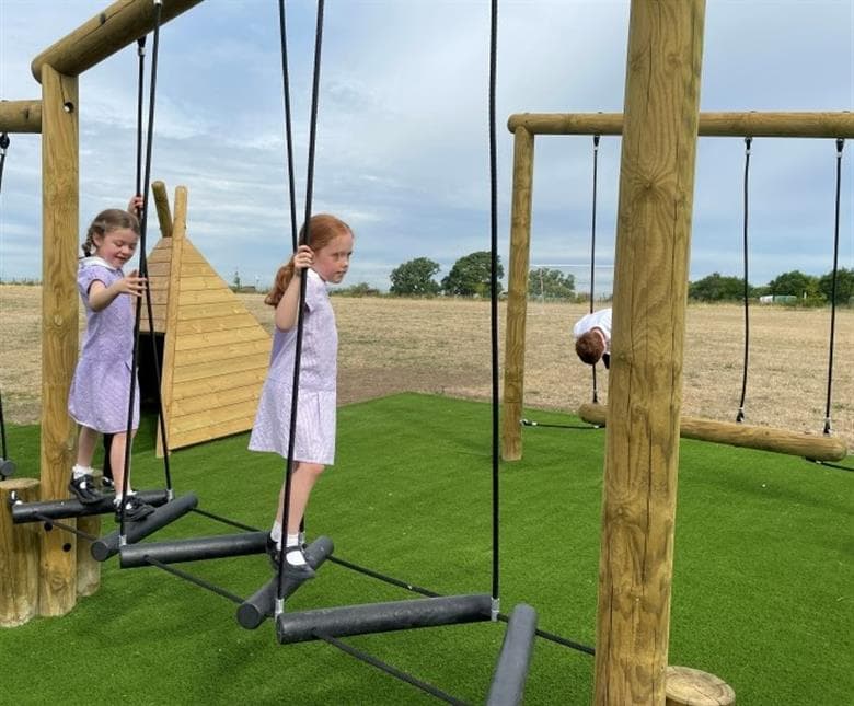 A group of girls climbing on the trim trail in their playground