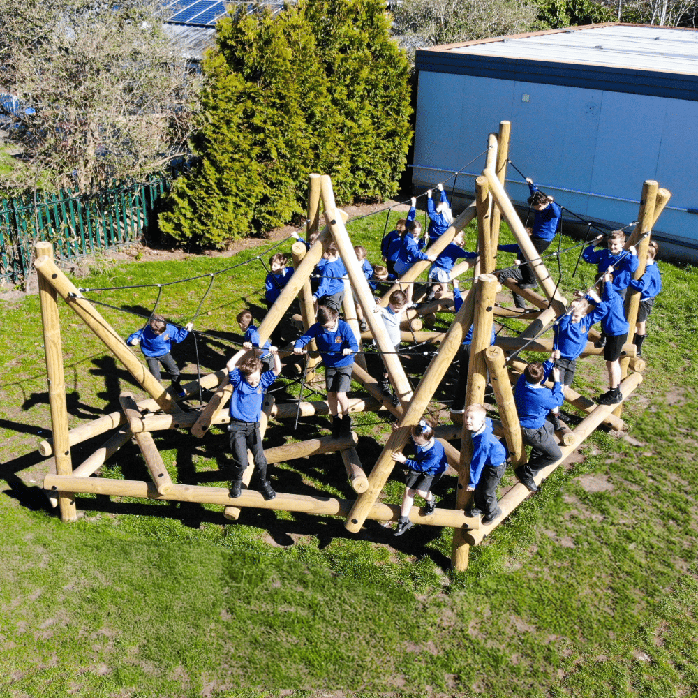 An overhead shout of a group of school children in blue jumpers playing on a large wooden climbing frame in a playground.