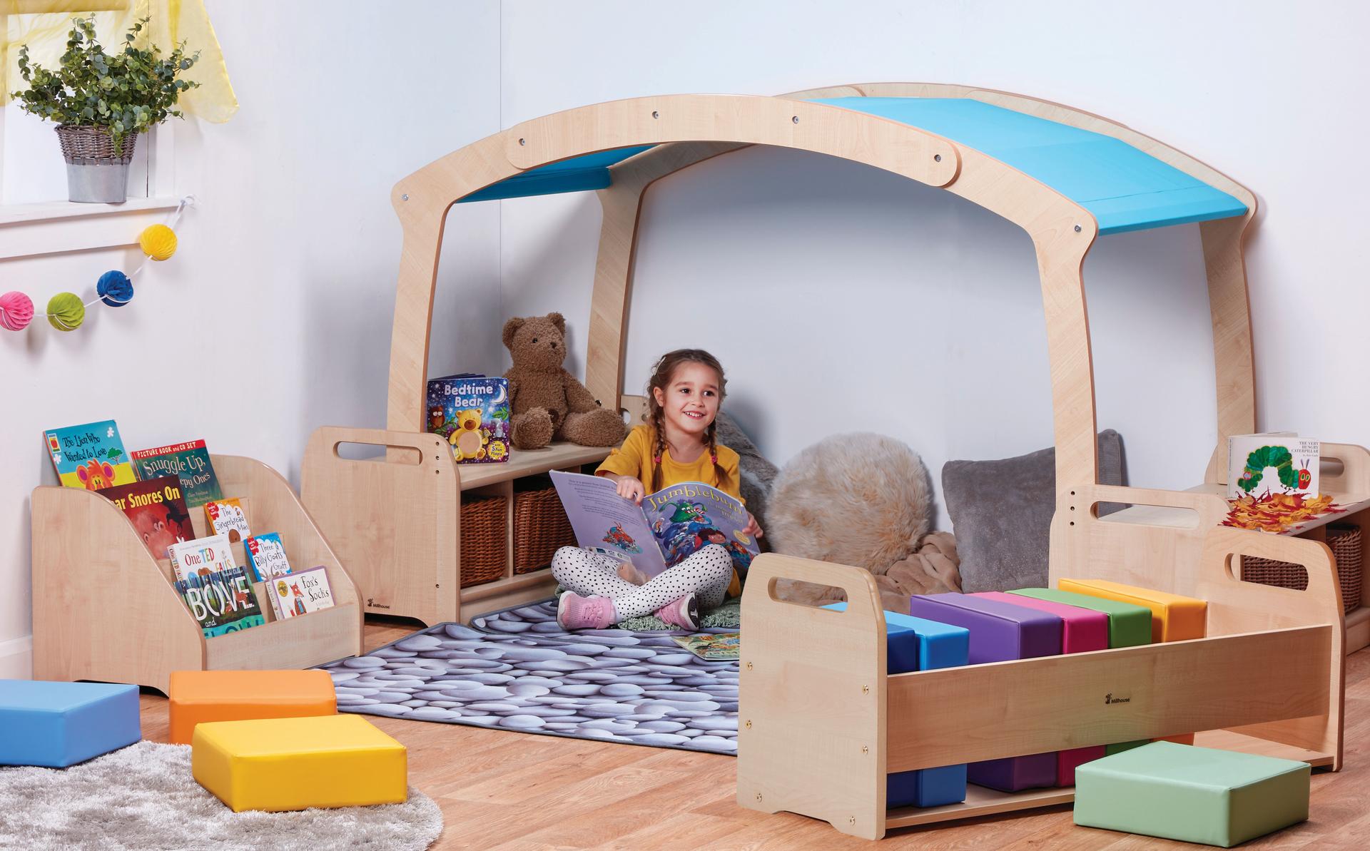 A young girl reading a book in the Mini Rainbow Reading Zone with Baskets, in a classroom.