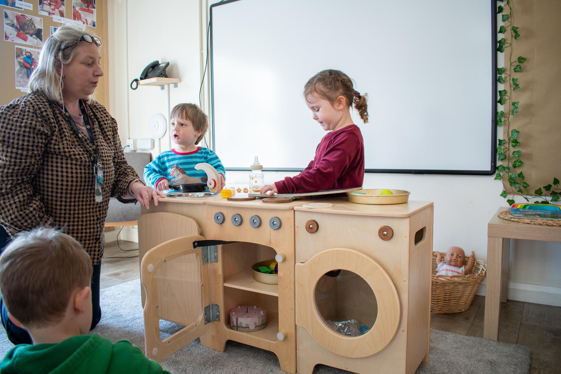 Nursery Staff helping children use their Millhouse kitchen set 