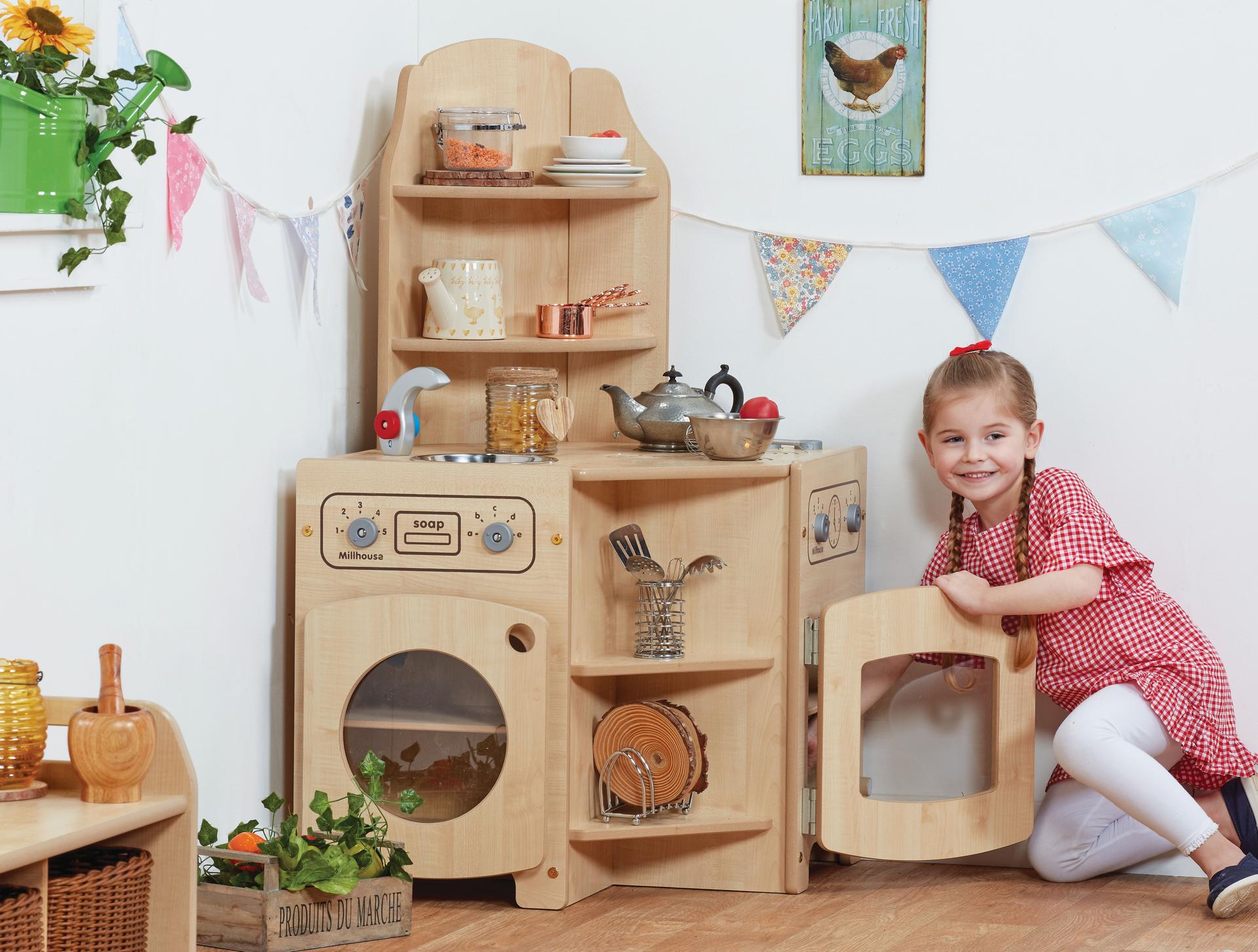 A wooden play-corner kitchen with a toddler putting something in the oven, in a nursery setting.