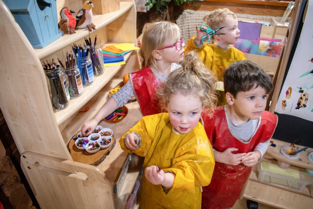Three children are looking at the camera as they hold a variety of different arts and crafts materials, as they stand next to the Millhouse Welsh Dresser.