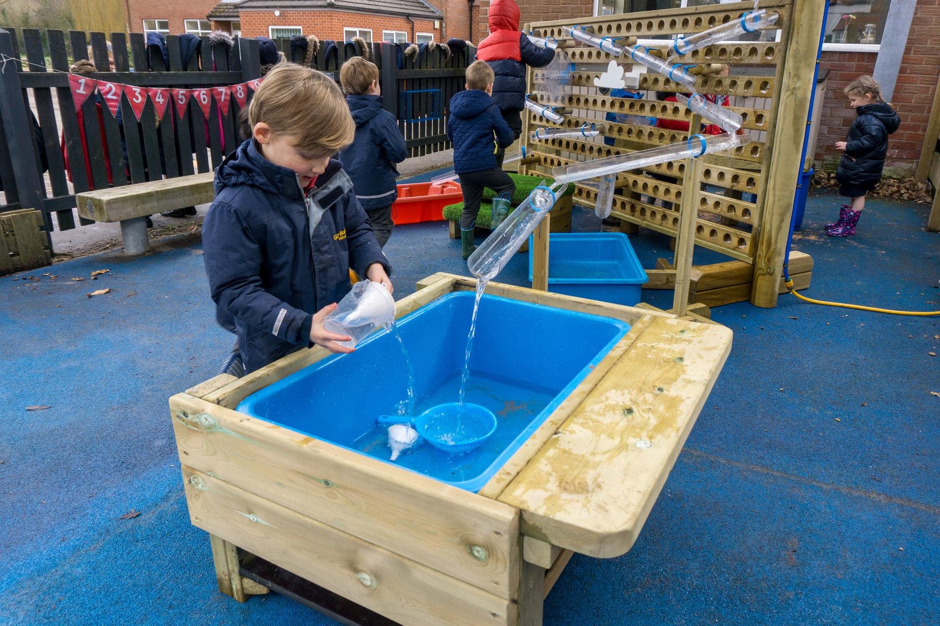 A little boy is pouring water from a jug into a tub.