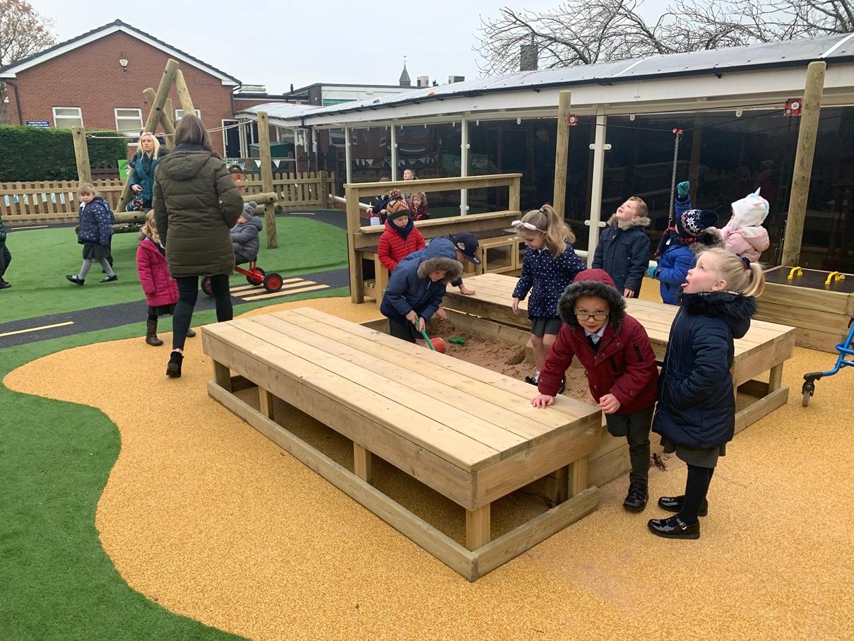 A large group of EYFS children are exploring the large covered sand box and are playing with the sand.