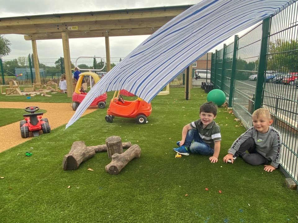 two little boys sit beneath a fabric canopy on the artificial grass surfacing and pose for a photo