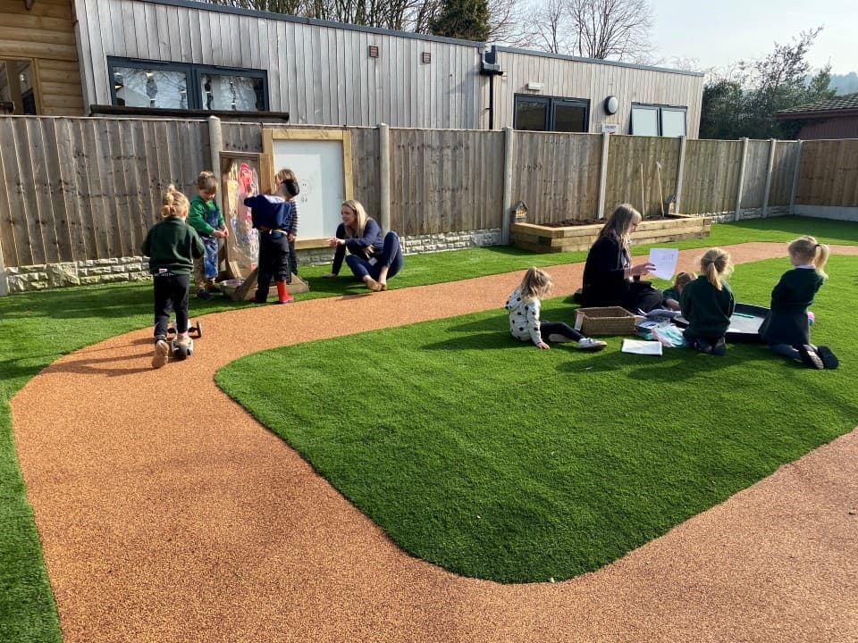 a teacher sits with two pupils on the artificial grass