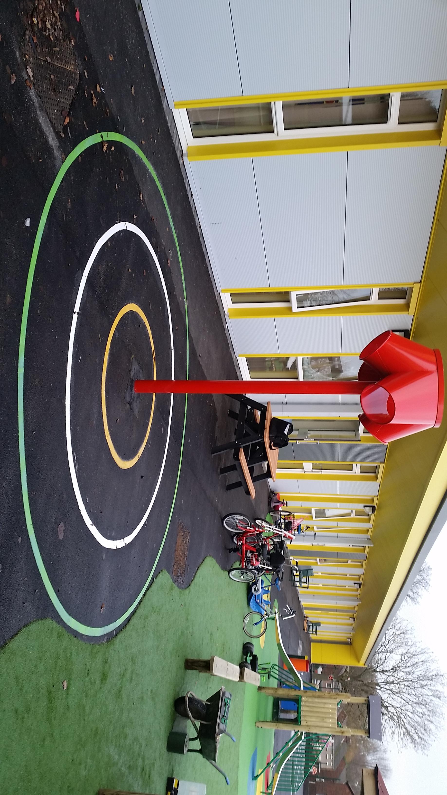 A red 3-way shoot that has been installed on a black wetpour playground with thermoplastic coloured circles.
