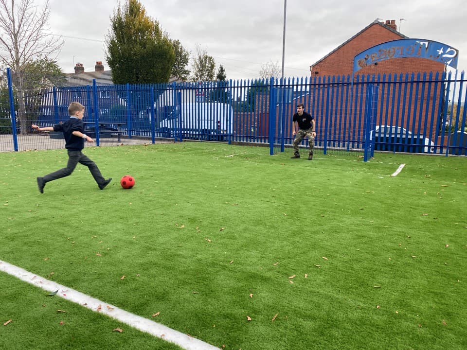 a child kicks a ball towards the goal end on the muga artificial grass surfacing