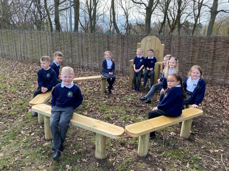 children sit on the perch benches of the story-telling circle and smile at the camera