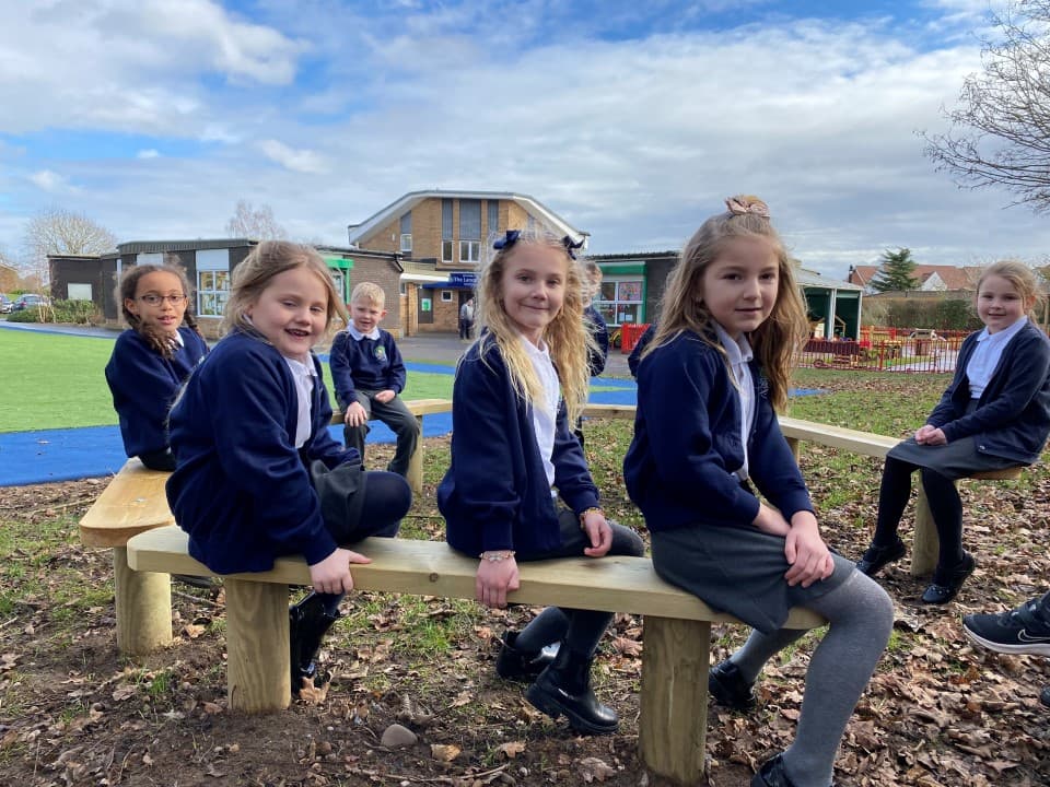 children sit in the story-telling circle on the perch benches and smile at the camera