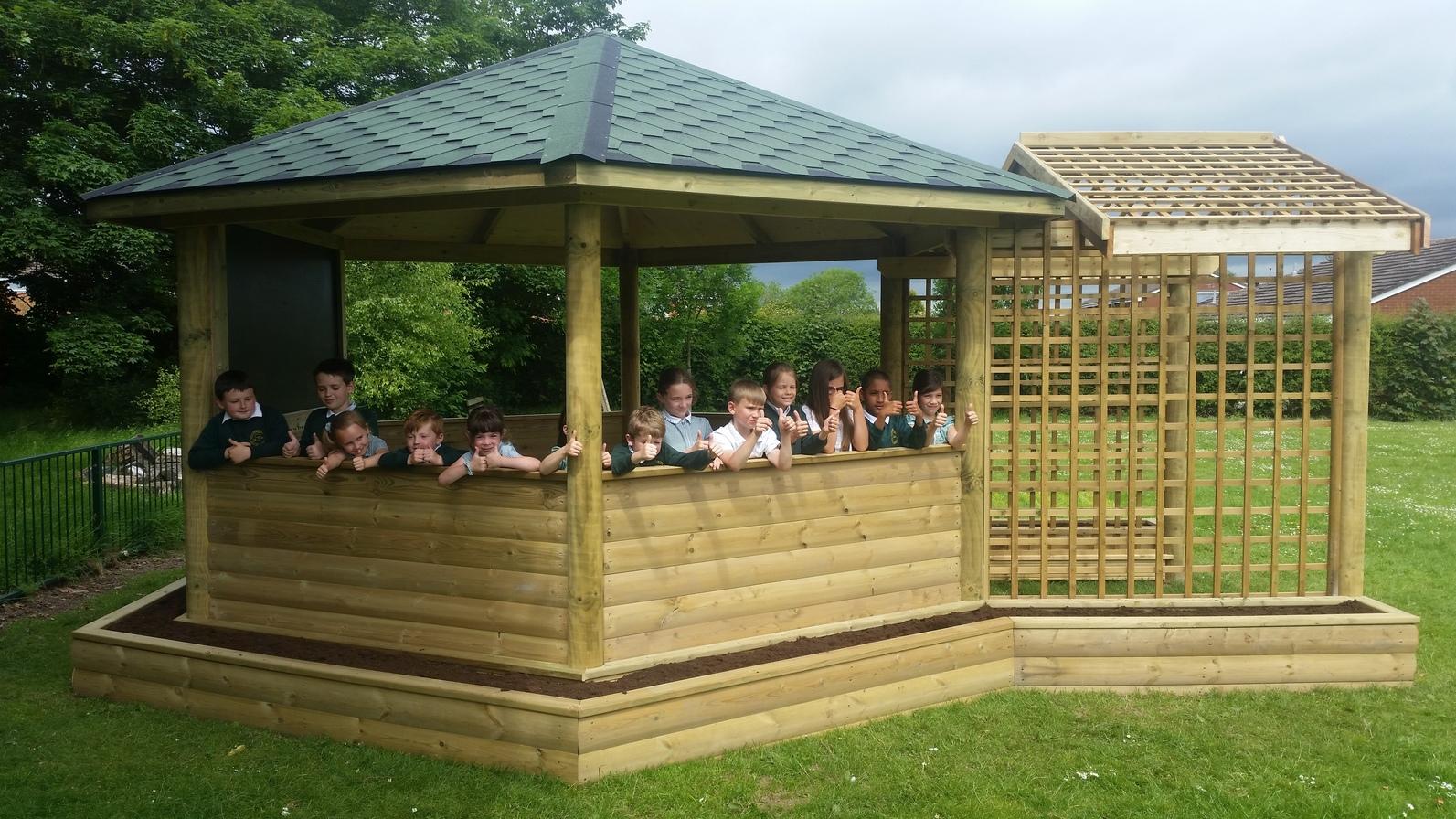 School children sitting in a wooden gazebo.