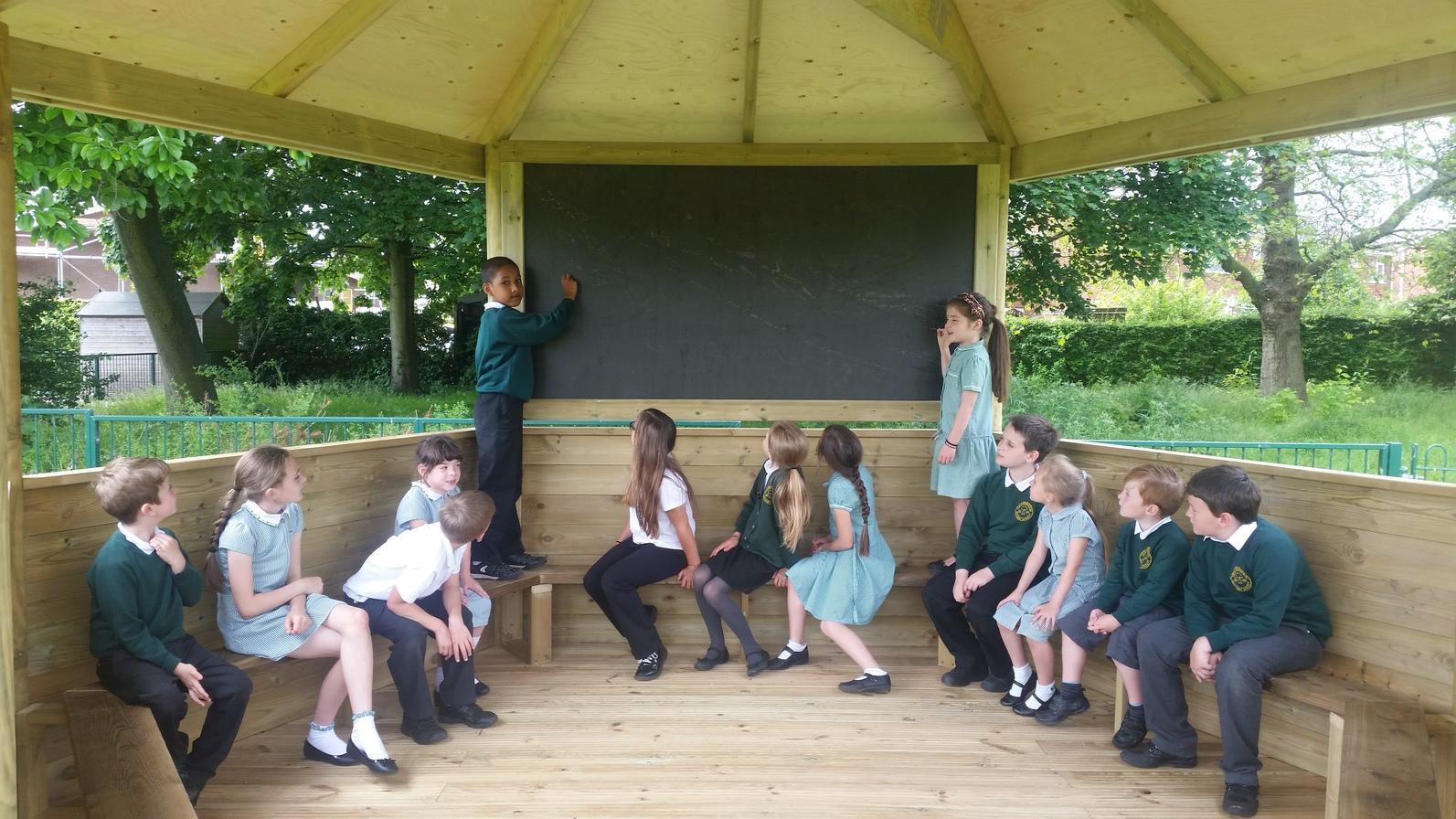 School children sitting in a wooden gazebo.