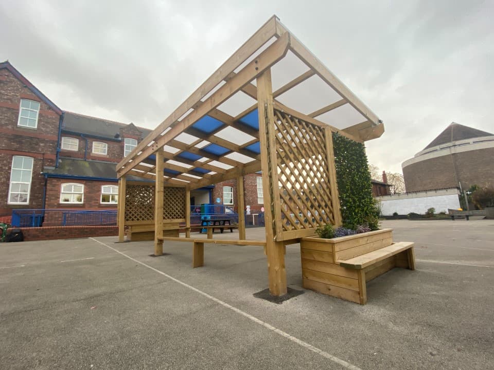 A freestanding timber canopy with planter benches and a polycarbonate blue and white roof