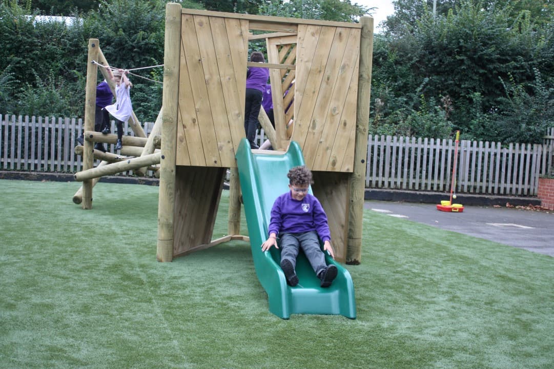 a child in purple school uniform slides down the green slide on the harter fell climber