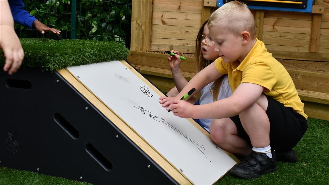 A young boy writing on the whiteboard slide in his playground 