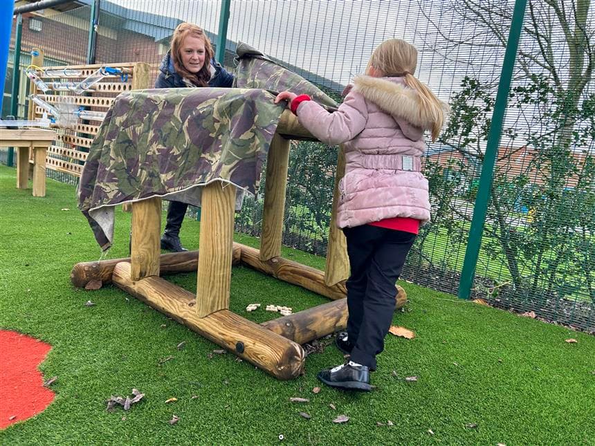 2 girls placing a den making sheet over a in out shape