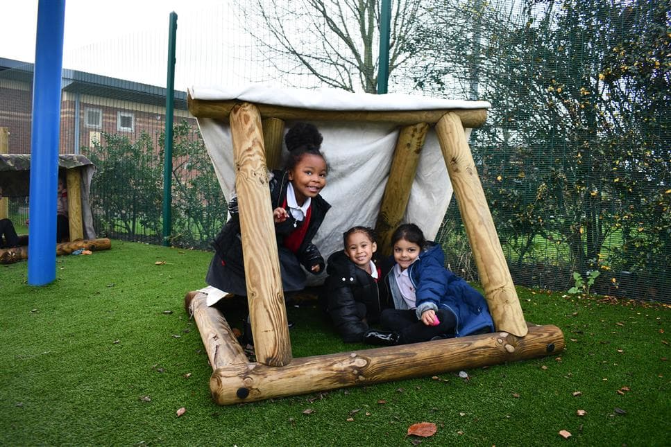 A group of children sat underneath a den in their playground