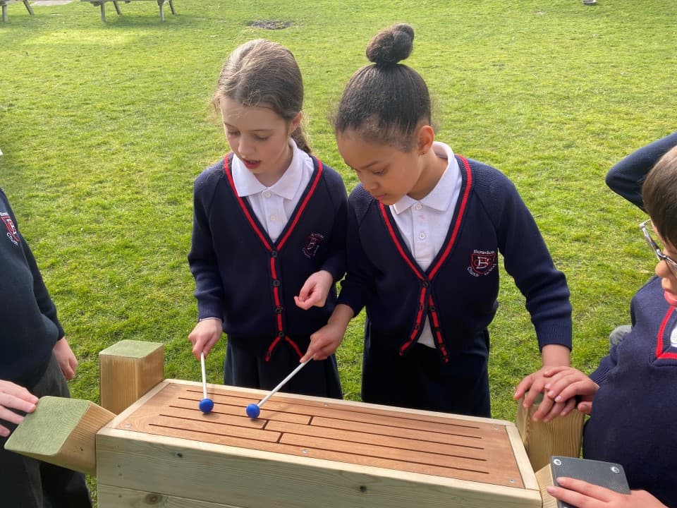 little girls share the drum stick as they play the tongue drum together