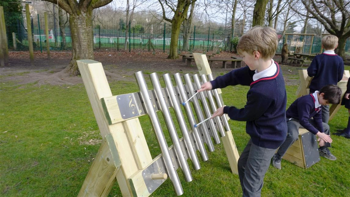 one young boy playing on the freestanding chimes in his primary school